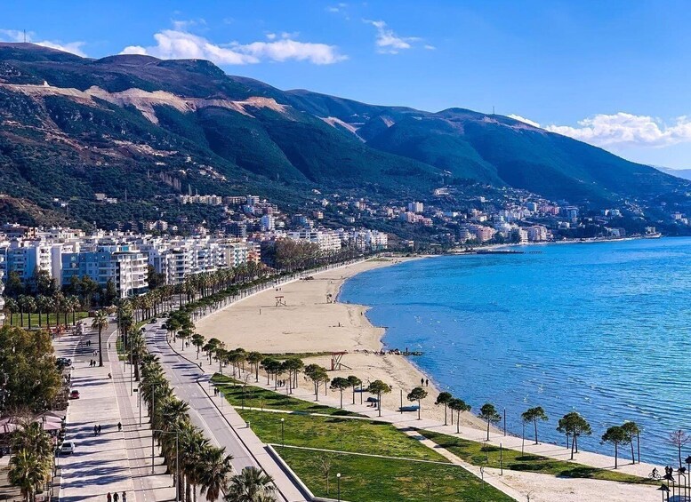 A coastal city with a beach, a promenade lined with palm trees, and mountains in the background. 4