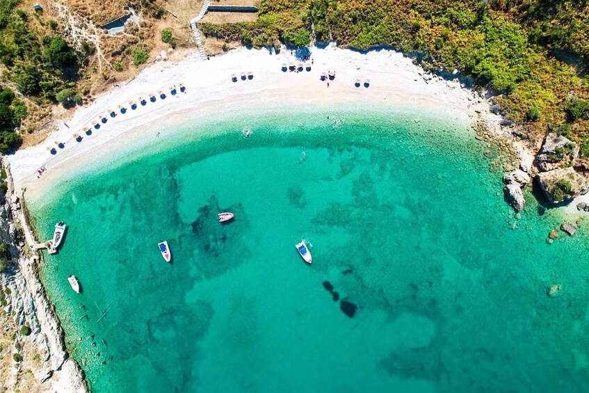 A coastal area with a clear turquoise sea, a sandy beach, and several boats anchored near the shore. 5