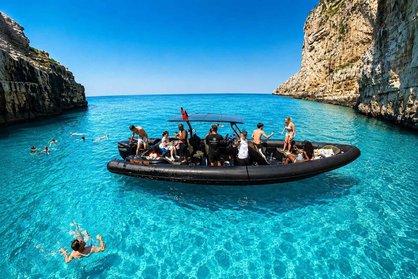A group of people on a boat in a clear blue sea with rocky cliffs. 2