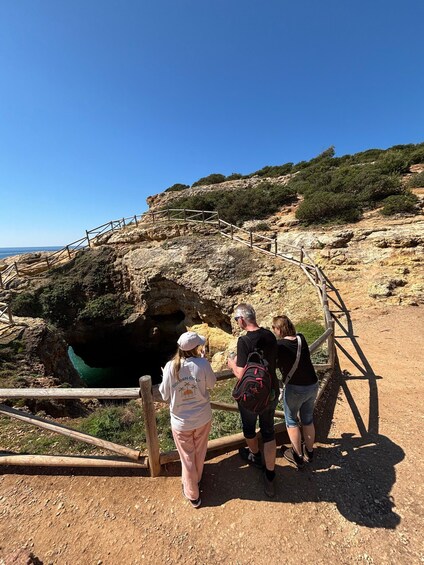 A group of people standing at the entrance of a cave with a wooden railing. 1