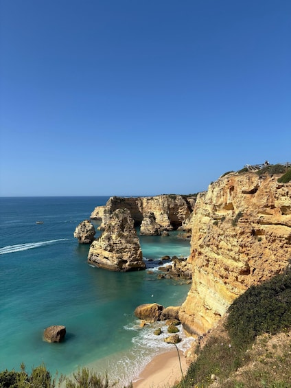 A coastal landscape with prominent rock formations, clear blue sea, and a sandy beach. 2