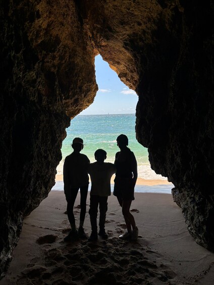 A silhouette of three people standing in a cave opening facing the ocean. 5