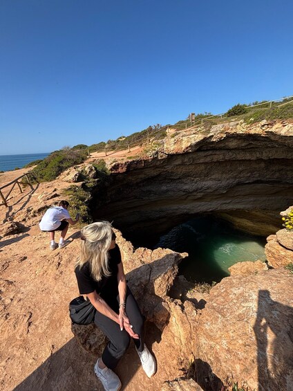 A person sitting on a rock by a cliff edge overlooking a body of water. 4