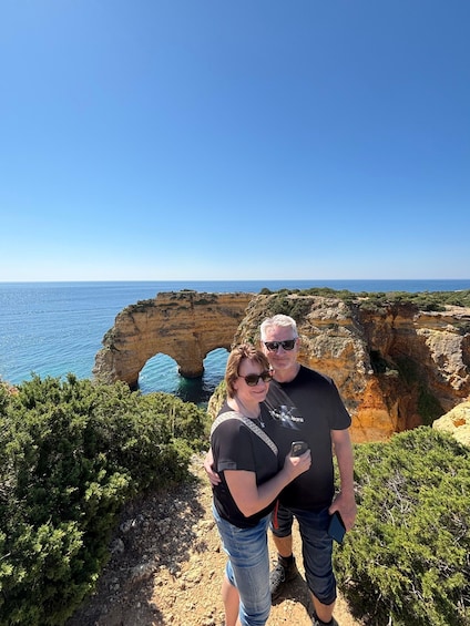 A couple standing on a rocky cliff overlooking a coastal landscape with cliffs and the sea. 1