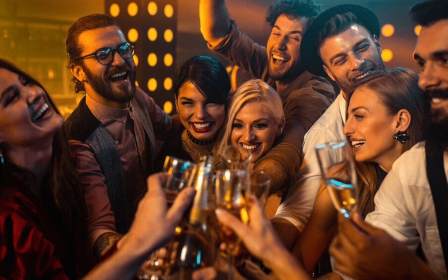 A group of people toasting with drinks in a dimly lit indoor setting. 3