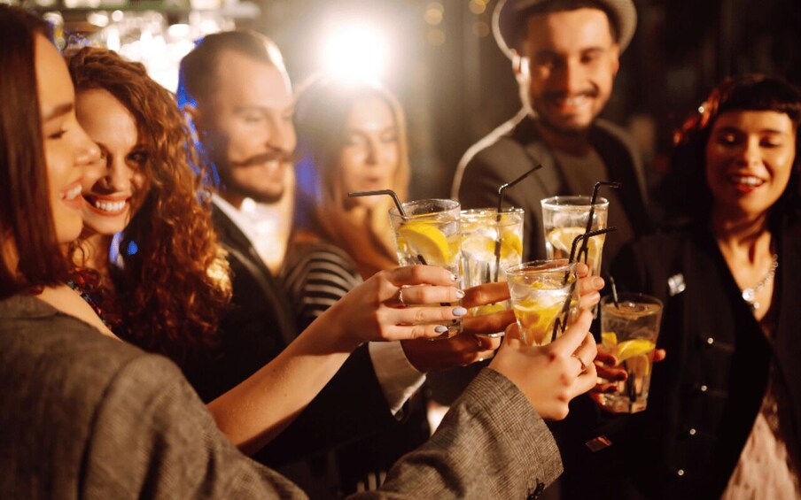 A group of people toasting with drinks that have lemon slices and straws. 2