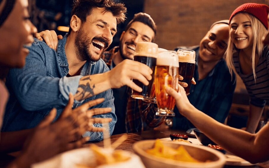 A group of people toasting with beer glasses at a table with food. 5