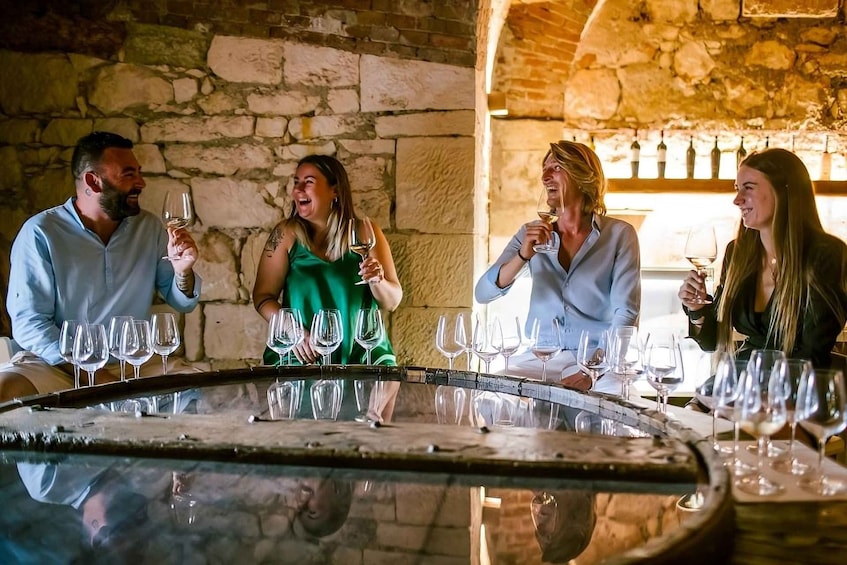 A group of people tasting wine at a rustic cellar with stone walls and a barrel. 1