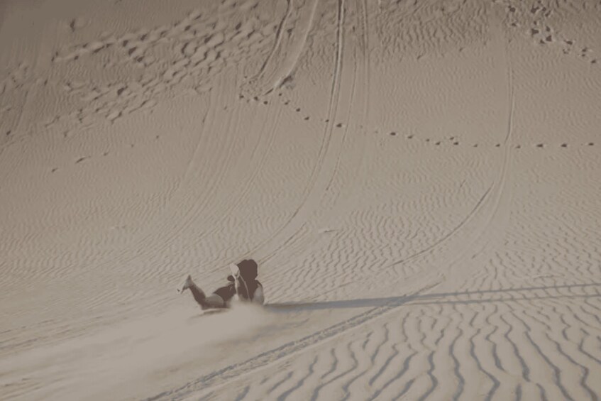 A person sledding down a sandy slope. 3