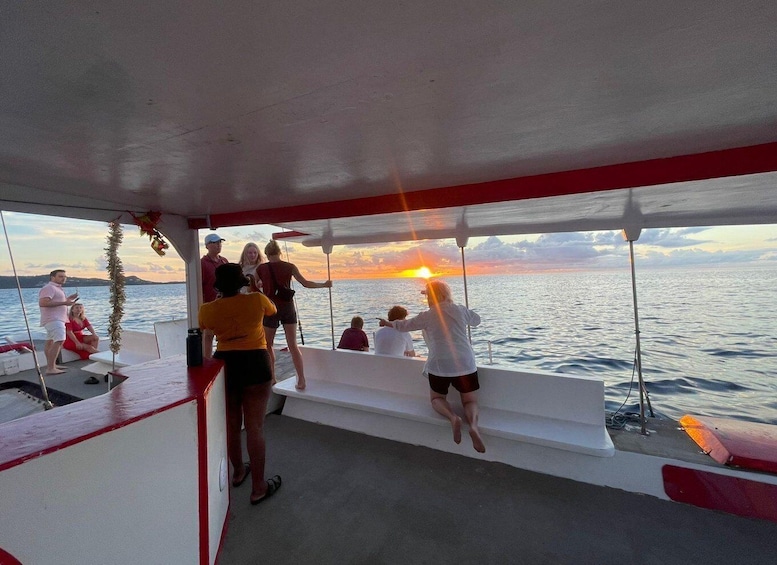A group of people on a boat during sunset, with the sun visible near the horizon. 1
