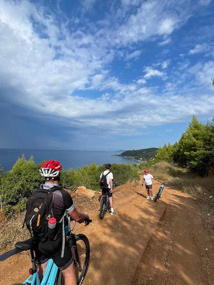 Three cyclists on a dirt path with a scenic view of the sea and hills in the background. 1