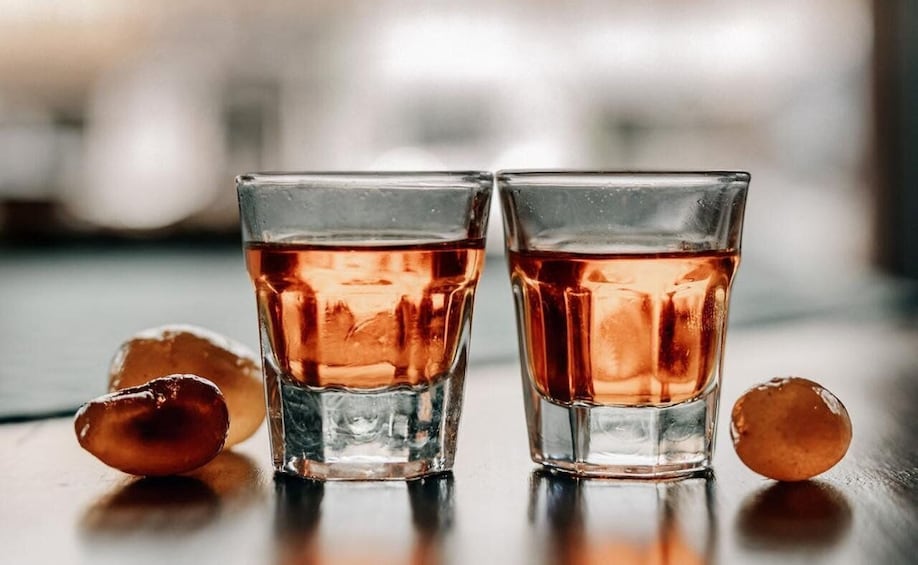 Two glasses of amber liquid with ice cubes on a reflective surface. 3