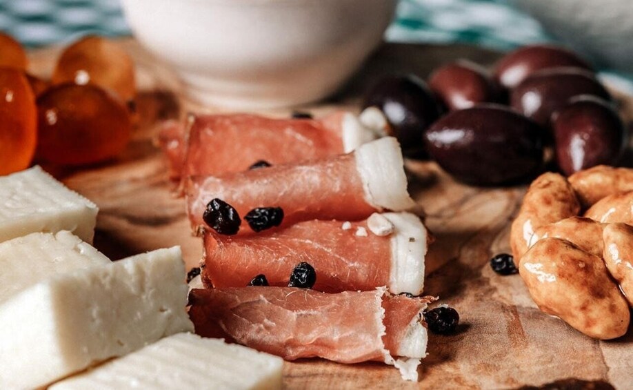 Sliced prosciutto, olives, nuts, and cheese on a wooden board. 2