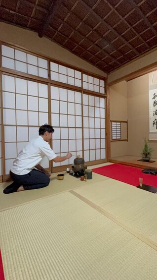A person performing a tea ceremony in a traditional Japanese room with tatami flooring and shoji screens. 5