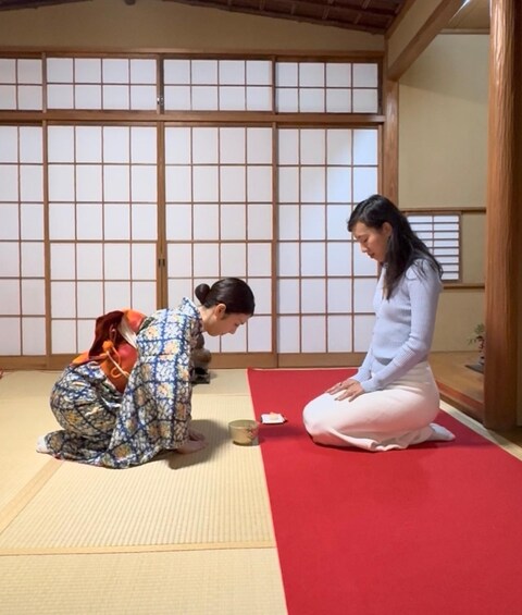 Two people in traditional Japanese attire performing a seated exercise on tatami mats in a room with shoji screens. 1