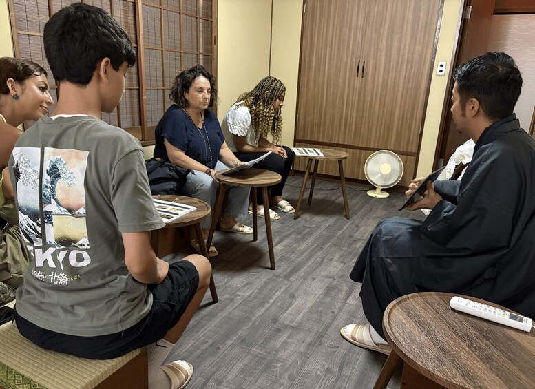A group of people seated in a room with wooden floors and furniture, engaged in a discussion or meeting. 2