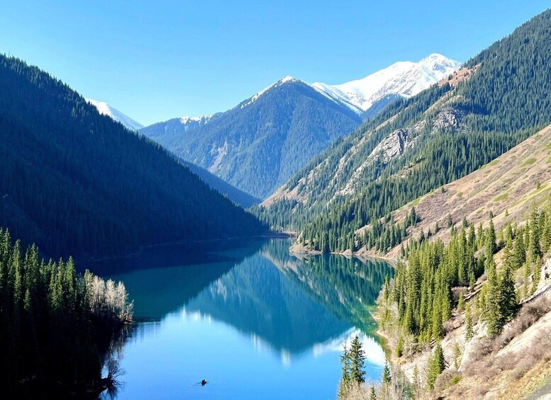 A calm lake surrounded by forested mountains under a clear sky. 4