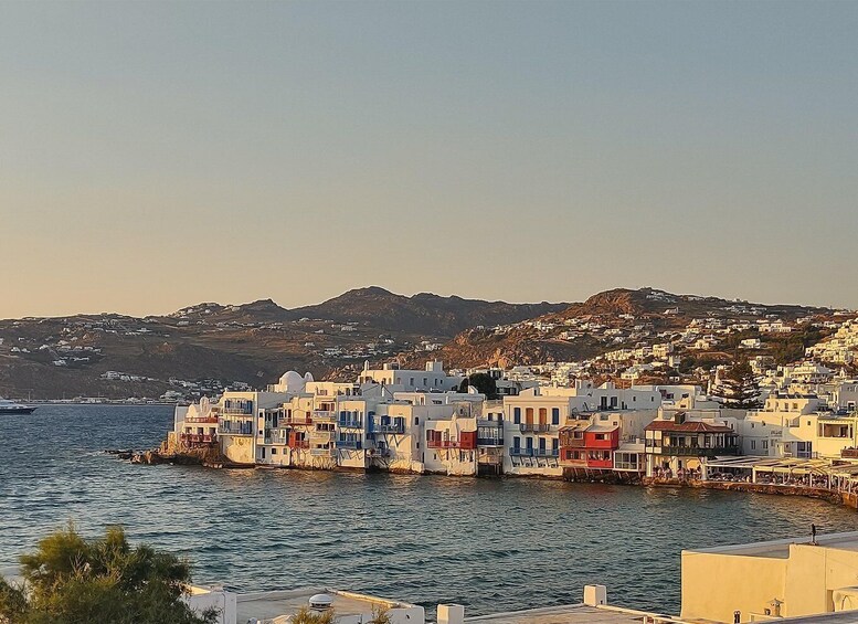 A coastal town with white buildings, a clear sky, and mountains in the background. 1