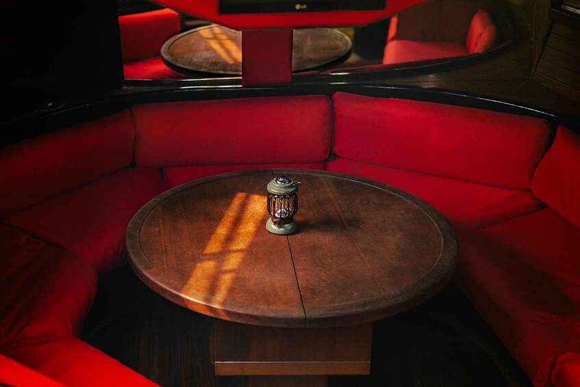 A red upholstered booth with a round wooden table and a decorative object in the center. 5