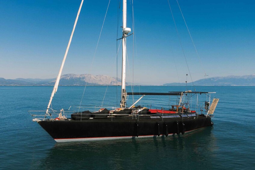 A black sailboat with a red stripe on the hull, anchored in calm waters with a mountainous landscape in the background. 4