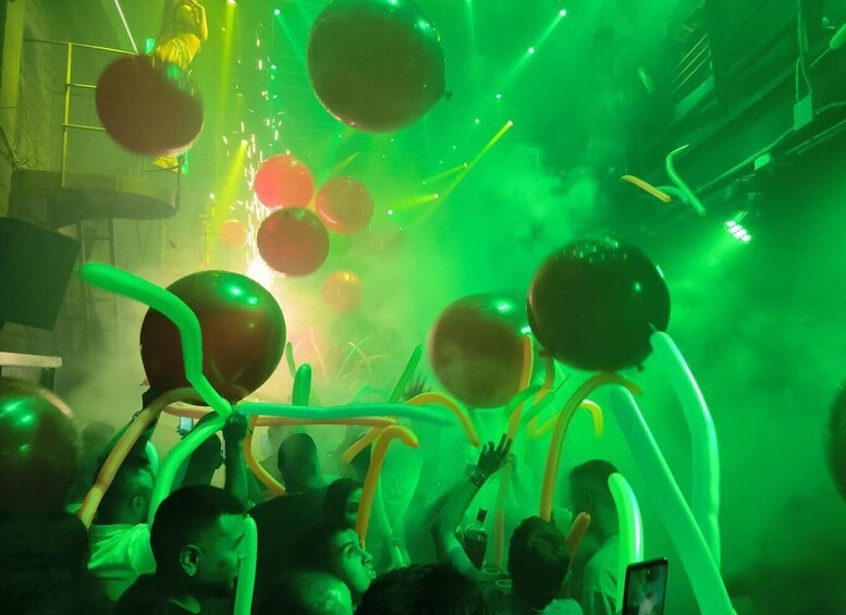 A crowded indoor event with green lighting and balloons. 3
