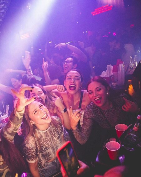 A group of people at a party with drinks and a phone in hand. 1