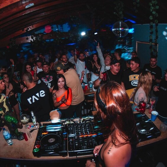 A crowded bar with people dancing and a DJ booth. 1