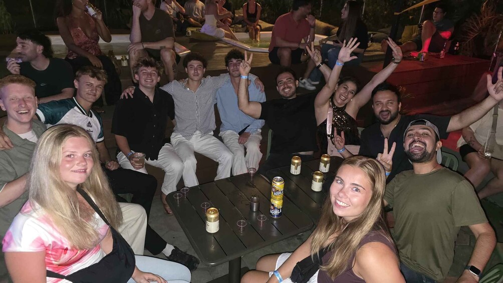 A group of people sitting around a table with drinks, some making peace signs. 2