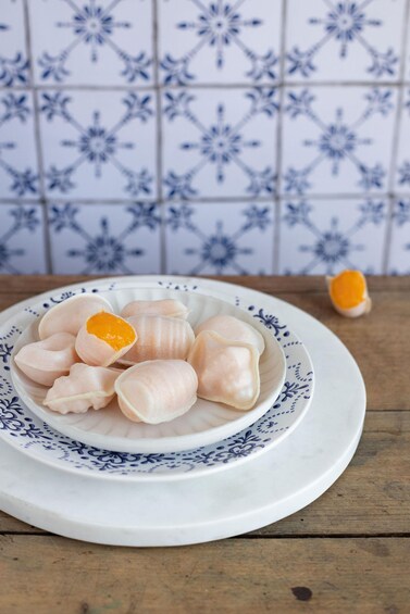 A plate of uncooked dumplings on a decorative plate with a blue pattern, set against a tiled wall with a blue floral design. 3