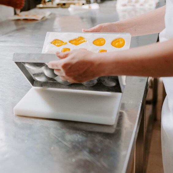 Hands placing yellow-colored dough into a muffin tin on a kitchen counter. 4