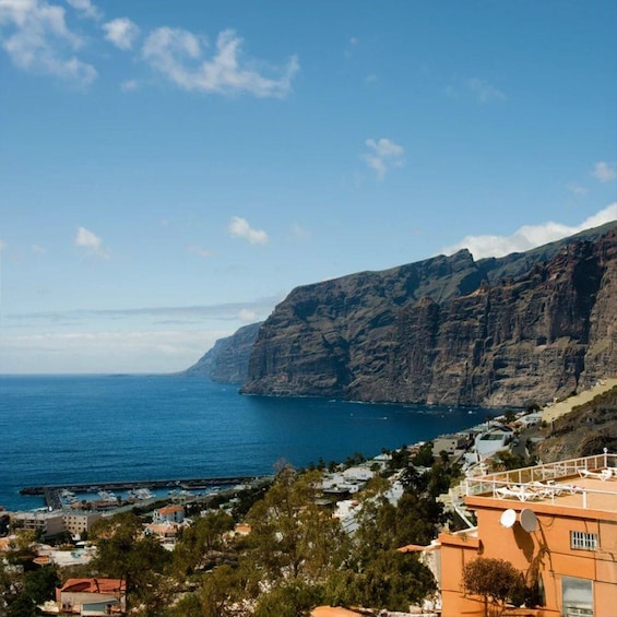 A coastal town with a prominent cliff, clear blue sea, and residential buildings. 1