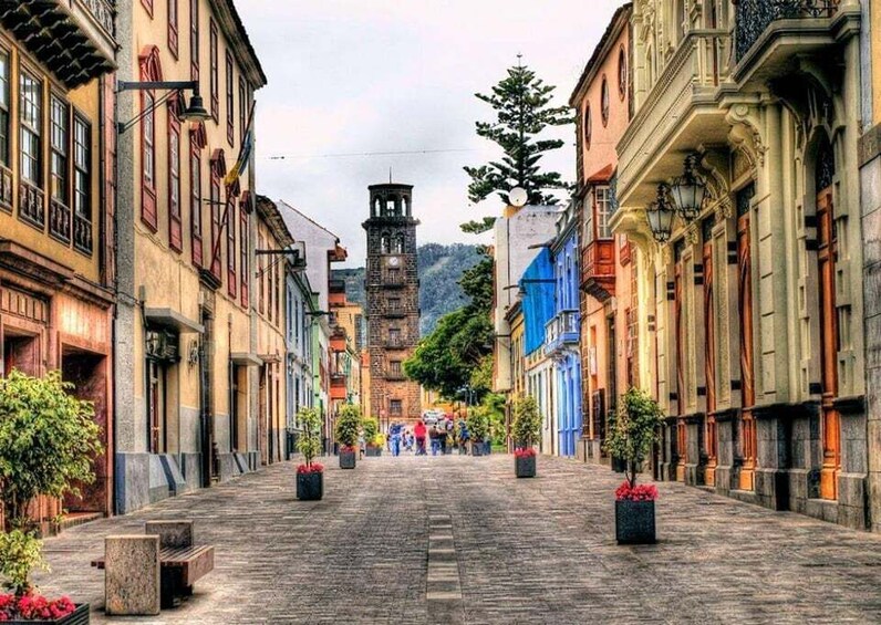 A cobblestone street lined with historic buildings, a clock tower, and potted plants. 2