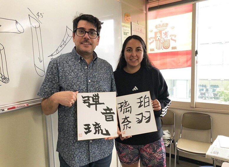 Two people holding signs with Japanese characters in a classroom with a whiteboard and a window with a red curtain. 4