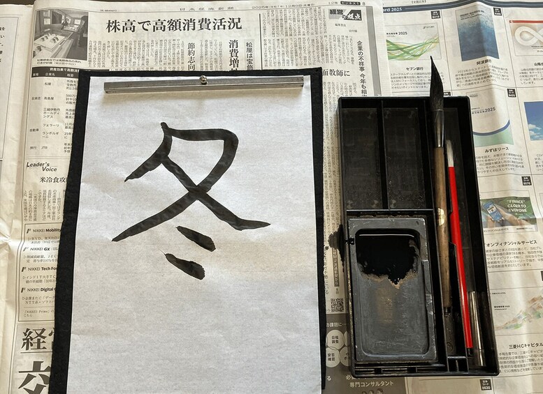 A calligraphy brush, ink, and paper with a large Chinese character on a newspaper background. 2