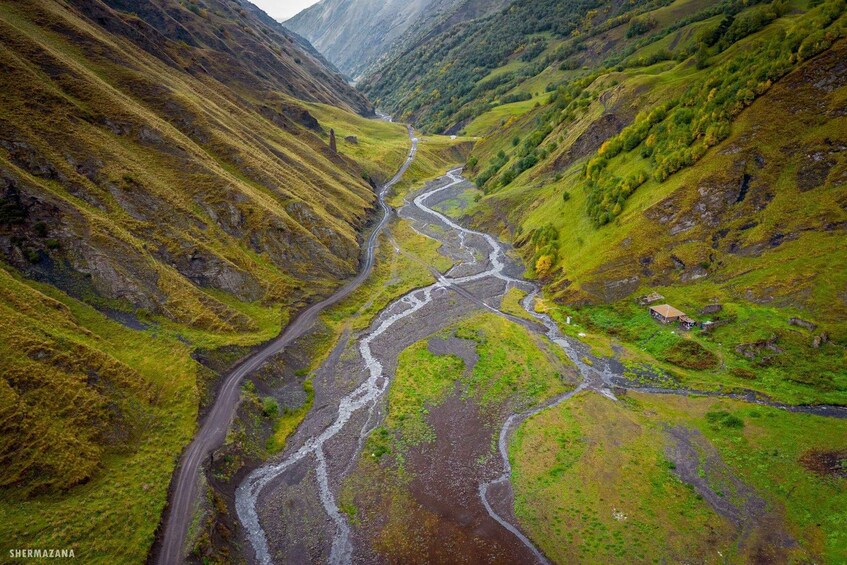 A winding river through a valley with a road and a small building. 4