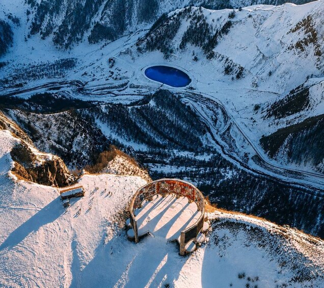 A snow-covered mountain landscape with a circular blue lake and a wooden bridge. 2
