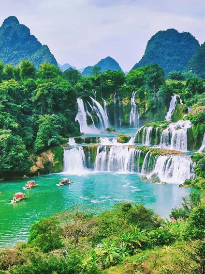 A multi-tiered waterfall surrounded by lush greenery and mountains in the background. 1