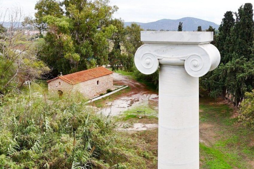 A white column with Corinthian capitals, a stone building with a red-tiled roof, and a mountainous backdrop. 1