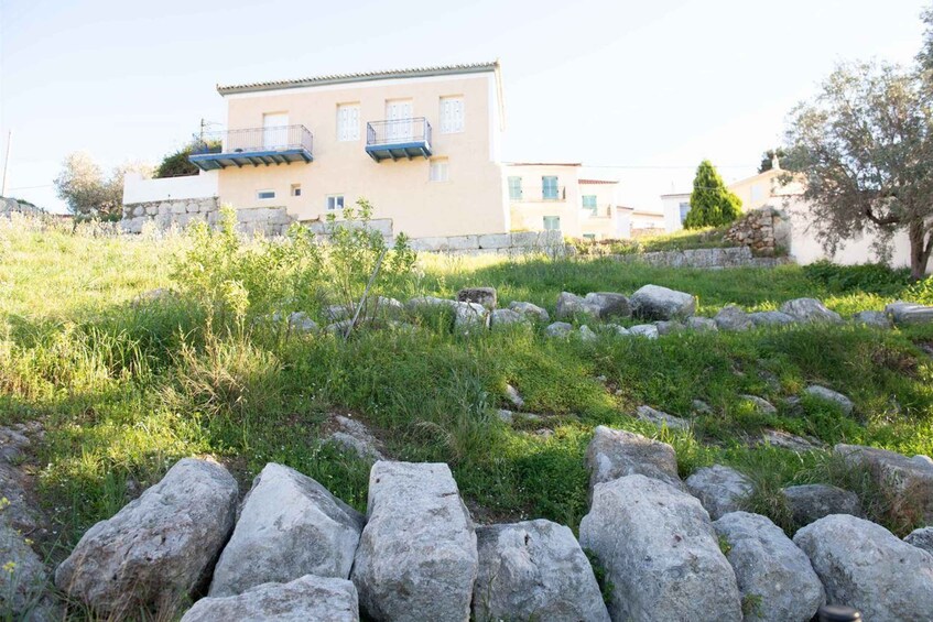A building with a light facade, stone wall, and a grassy area with large rocks. 5