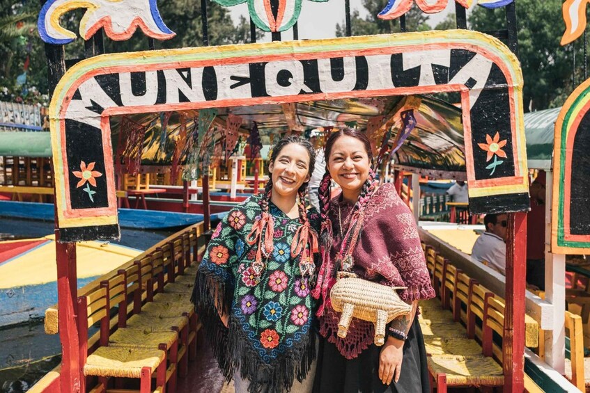 A colorful, hand-painted archway with 'UNQUESTA' written on it, leading to a covered seating area with wooden benches. 3