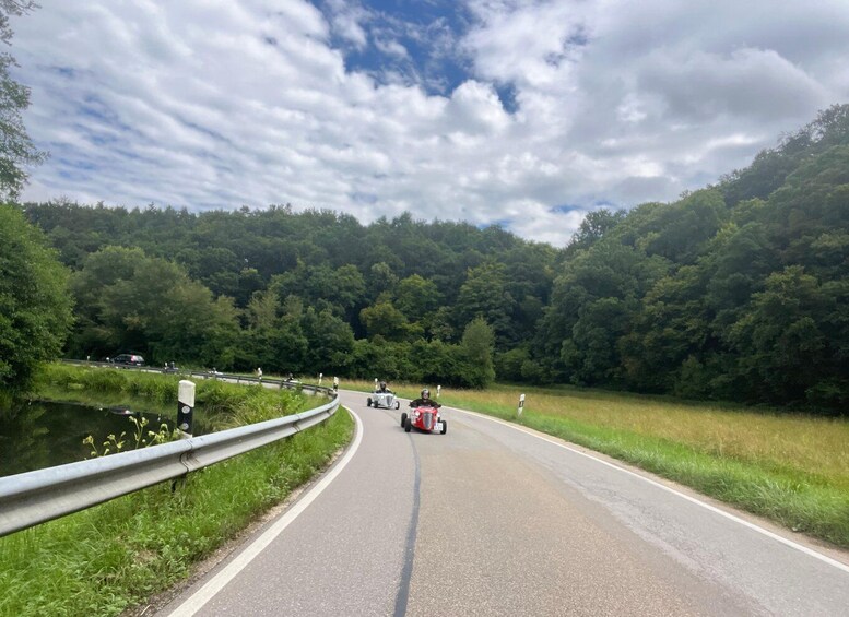 A road curving through a forested area with a body of water on one side and a guardrail on the other. 2