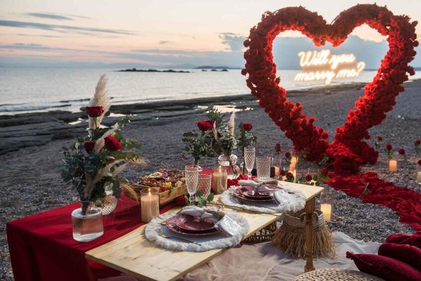 A romantic outdoor dinner setup with a heart-shaped floral arrangement, a table with plates and candles, and a scenic beach backdrop. 5