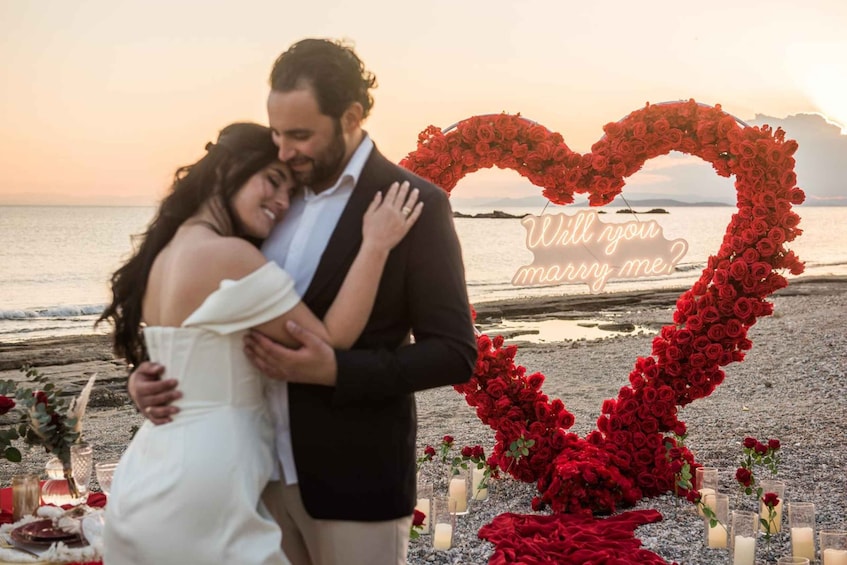 A couple embracing in front of a heart-shaped floral arrangement with a sunset in the background. 2