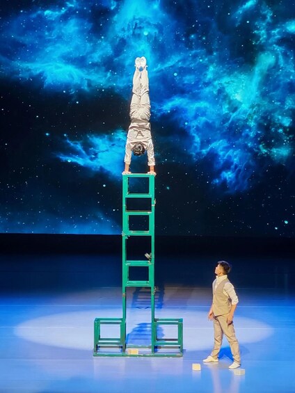 A person performing a handstand on a green ladder with a starry nebula background. 4