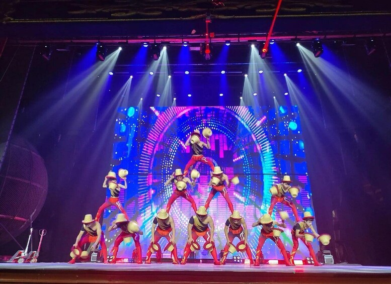 A stage performance with dancers in hats and red outfits, illuminated by stage lights and a digital backdrop. 1