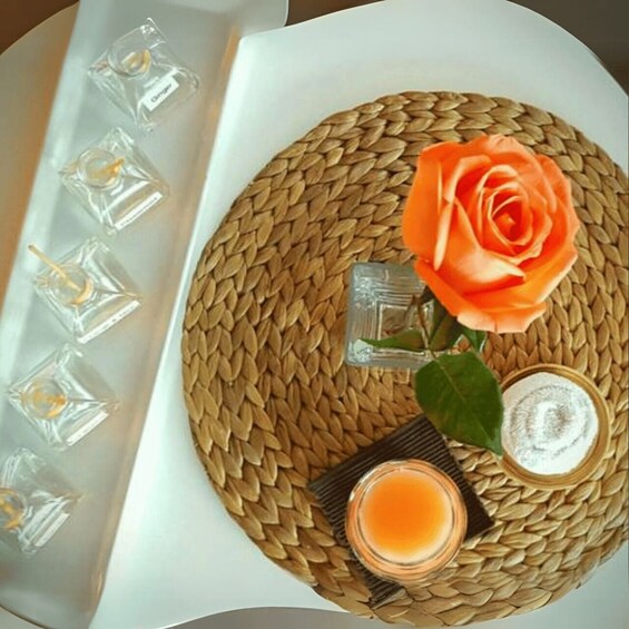A woven mat with a rose, candle, and glass containers. 4