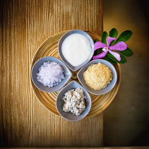 A wooden table with four bowls containing different food items and a purple orchid. 2