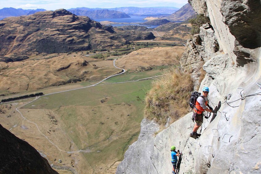A person rappelling down a steep cliff with a valley and mountains in the background. 2