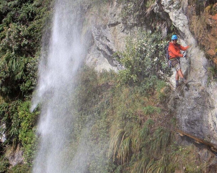 A person rappelling down a cliff with a waterfall in the background. 4