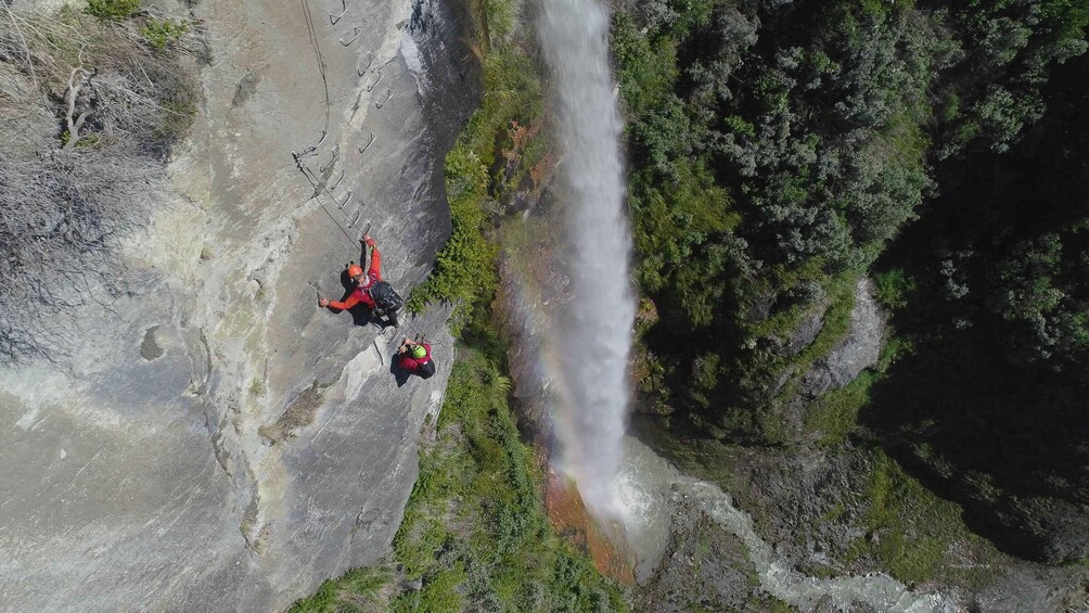 Two climbers on a rock face with a waterfall in the background. 1